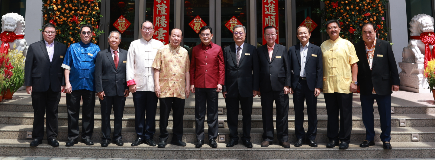 Group of eleven men in formalwear standing on steps with Chinese New Year decorations.